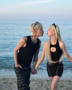 two women standing on the beach with their hands in each other's pockets and looking into each others eyes