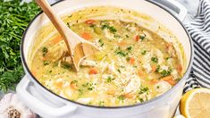 a white pot filled with chicken and rice soup next to sliced lemons, parsley and garlic