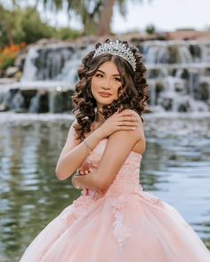 a woman wearing a tiara standing in front of a waterfall with her arms crossed