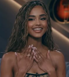 a smiling woman with her hands together in front of her chest and wearing gold jewelry