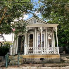 a small white house sitting on the side of a road next to a fence and trees