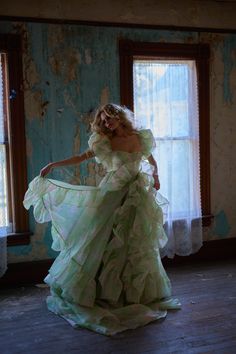 a woman in a green dress is standing by a window