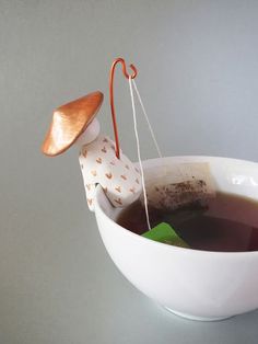 a tea bag in a white bowl filled with black liquid and an orange hook hanging from it's end