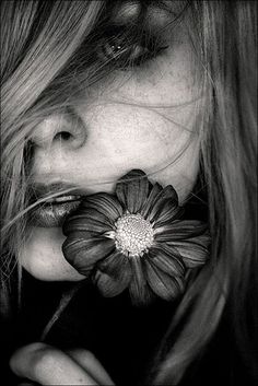 a woman with long hair holding a red flower in her mouth and looking at the camera