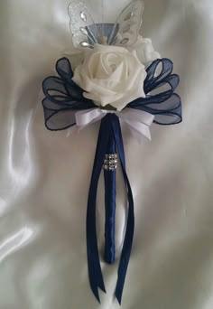 a white rose and blue ribbon boutonniere on a satin material background,