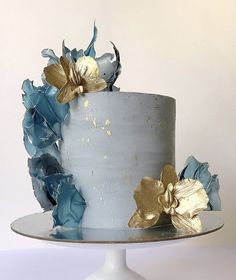 a white and blue cake with gold flowers on top is sitting on a silver platter