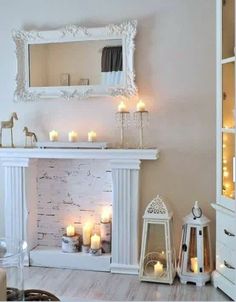 a living room filled with lots of white furniture and candles in front of a fireplace