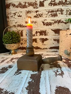 a lit candle sitting on top of a wooden block next to a potted plant