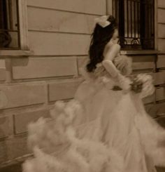 an old photo of a woman in a wedding dress walking down the street with her hand on her face