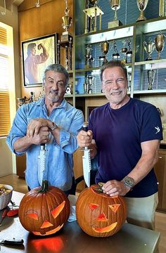 two men standing next to each other holding knives and carved pumpkins with faces on them