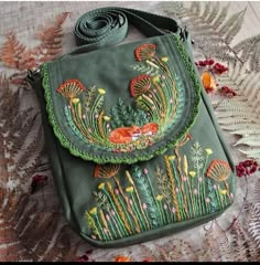 a green purse with embroidered flowers and plants on the front, sitting on a lace tablecloth