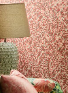 a lamp sitting on top of a table next to a wallpaper covered in leaves