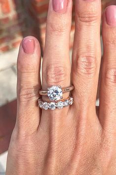 a woman's hand with two wedding rings on her left and the other hand holding an engagement ring