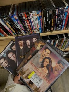 a person holding several dvds in front of a bookshelf