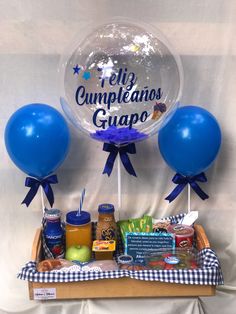 a basket filled with blue balloons and confetti in front of a sign that says, el cumpleanos gupo