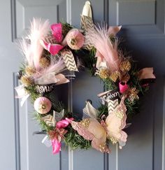 a wreath with pink flowers and feathers hanging on a door