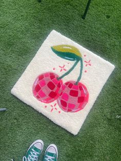 a pair of tennis shoes sitting on the ground next to a rug with two cherries painted on it