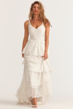 a woman is wearing a white dress with ruffles on the bottom and spaghetti straps