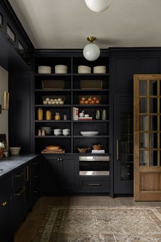 a kitchen with black cabinets and an area rug in front of the door that leads to another room