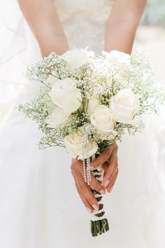 a bride holding a bouquet of white roses and baby's breath in her hands