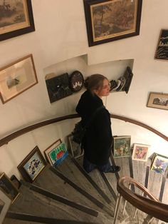 a woman standing on the top of a spiral staircase next to pictures and framed photographs