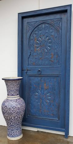 a blue vase sitting in front of a door with an ornate design on it's side