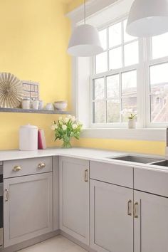 a kitchen with yellow walls and white cabinets is pictured in this image, there are flowers on the window sill