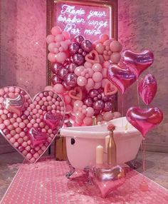 a bathtub filled with lots of pink balloons and heart shaped balloons in front of a sign