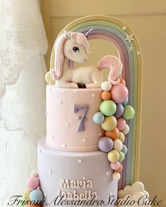 a pink and white cake with a unicorn on it's top is surrounded by balloons