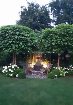 an outdoor fire pit surrounded by lush green trees and white hydrangeas in the foreground