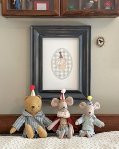 three stuffed animals sitting on top of a bed in front of a framed picture frame