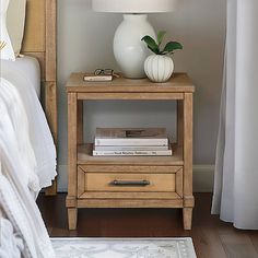 a white vase sitting on top of a wooden table next to a night stand with books