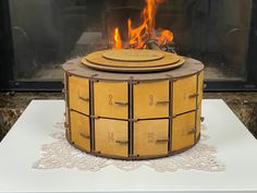 a wooden box with fire in it sitting on top of a white table next to a fireplace