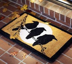 a door mat with two black birds on it and leaves scattered around the area next to it