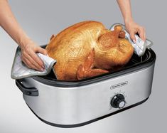 a person is removing a turkey from an electric roaster with a towel on it