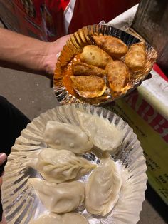 a person holding a plate with dumplings and sauce on it next to another plate filled with dumplings