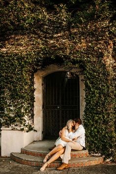 two people sitting on steps in front of a building with ivy growing up the walls