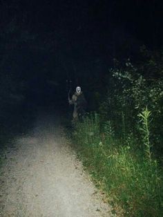 a person walking down a dirt road at night with a flashlight in their hand and ghost mask on