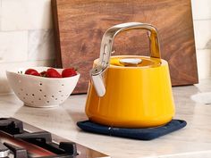 a yellow kettle sitting on top of a counter next to a bowl of strawberries