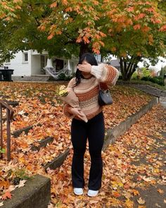 a woman standing in front of a tree with leaves on the ground and covering her eyes