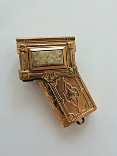 an antique gold brooch with a small rectangular object in the center, on a white background