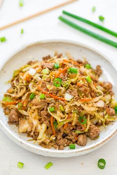 a white plate topped with meat and veggies next to chopsticks on a table