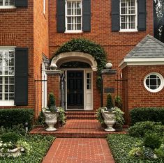 a brick house with black shutters and two large planters on the front door