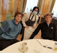 three people sitting at a table with masks on and one person wearing a face mask