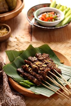 there are many skewers on the plate with meat and vegetables in bowls behind it