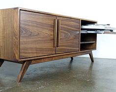 a wooden cabinet with two doors and some drawers on the bottom, in an empty room