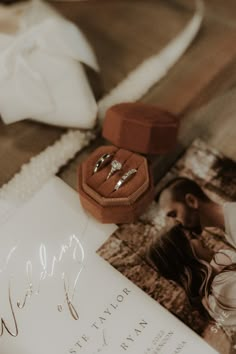 an open ring box with two wedding rings on top of it next to other items