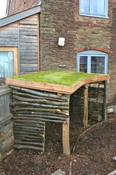 a wooden structure with grass on top in front of a brick wall and building next to it