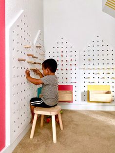 a young boy sitting on a stool in front of a wall with pegs and wooden letters