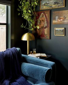 a living room with green plants and pictures on the wall, blue velvet chair in foreground